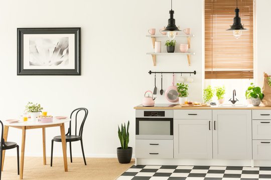 Industrial lamps and black dining chairs in a white kitchen interior with a modern oven and breakfast food