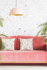 Pastel lamp above pink couch with patterned cushions in living room interior. Real photo