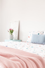 Pink blanket on bed with patterned sheets and blue cushion in bedroom interior with flowers. Real photo
