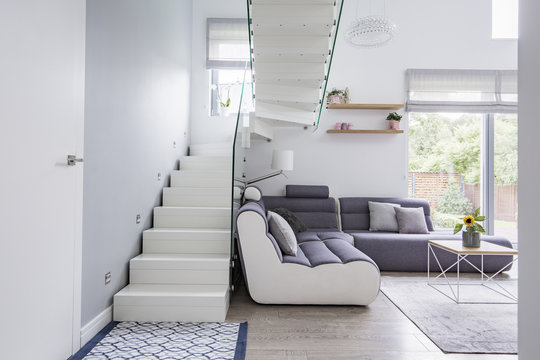 Large, modern sofa in a white living room interior with natural light and stylish staircase with glass barricade