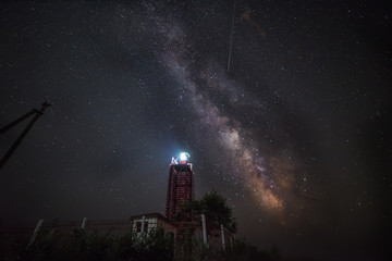 Night photo. The Milky Way and the falling stars of the Perseid meteor shower in August over the coastal lighthouse.
