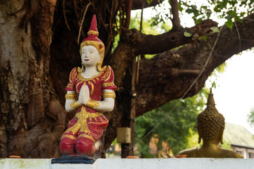 Small stone red and gold statue Buddha near to temple on a background of tree. Chiang Mai, Thailand.