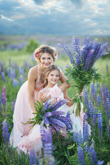 Mother and daughter gathering lupine flowers in beautiful field on sunset. Beautiful girl in violet dress holding a lupine at sunset on the field. The concept of nature and romance.