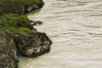Gloomy view from above on rocky sinuous riverbank. Dark green of water. Eerie atmosphere in overcast rainy weather in cinematic faded tones. Landscape with shore of river in horror style.