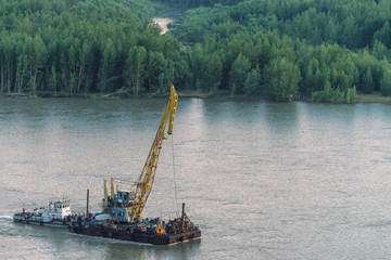 Beautiful river landscape with green shores and ship with copy space. Towboat tows barge with crane...