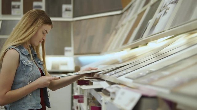 Serious woman looking for parquet to lay in the house. Carefully choosing among parquet samples in the store. Building supplies.