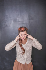 Beautiful teacher with headache on the blackboard background