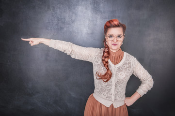 Serious woman teacher pointing out on chalkboard background