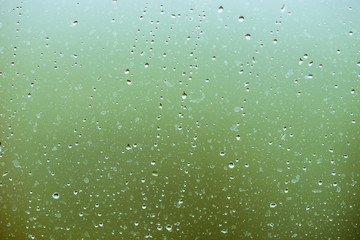 Dirty glass with drops of rain. Raindrops on green clear bokeh background. Greenery outside window. Droplets and stains close up. Detailed transparent texture in macro.