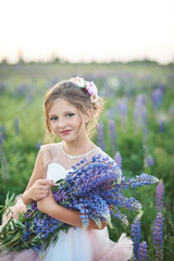 Fototapeta premium Beautiful girl in pink dress holding a lupine at sunset on the field. The concept of nature and romance. Happy childhood