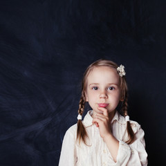 Сurious child thinking. Little girl on chalk board background with copy space. Back to school, kid...