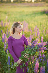 Beautiful pregnant woman in violet dress holding a lupine at sunset on the field. The concept of nature and romance.