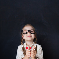 Сurious Girl in Glasses Showing Hands with Thumb Up and Smiling on Chalk Board Background. Child...