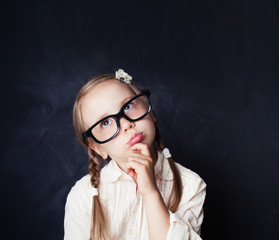 Child thinking. Little girl in glasses on chalkboard background with copy space.  Back to school,...