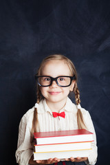 Pretty child girl with stack of books on chalkboard background. Back to school, elementary school...