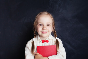 Smiling girl with red book on empty chalkboard background with copy space. Child portrait