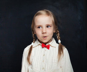Surprised schoolgirl on empty chalkboard backgroung with copy space