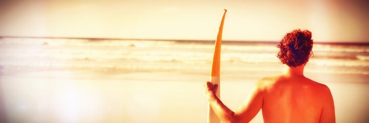 Rear view of shirtless man holding surfboard at beach