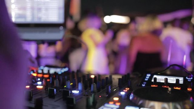 consolle e pulsanti di un deejay in un locale di ballo notturno, persone che ballano sfuocate sullo sfondo