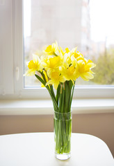 Posy of bright yellow daffodils on white wooden table.