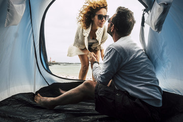 couple of caucasian woman and men 40 years old in love camping at the beach in tropical place, living near the ocean and enjoying vacation in tent. kiss and lighthouse in background