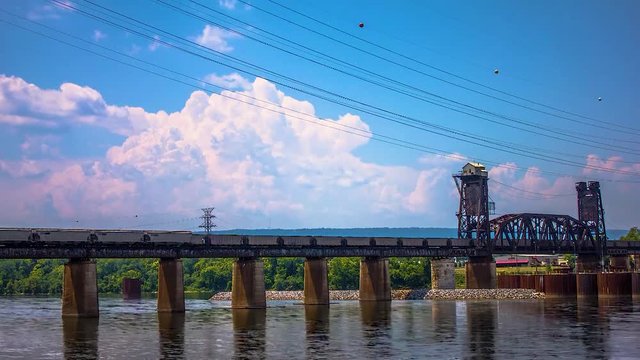 Time lapse of trains going over river trestle as thunderclouds build in the background.