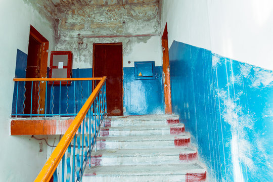 A staircase leading to the last floor of a dilapidated building. Blue peeling paint on the walls and leaking ceiling.