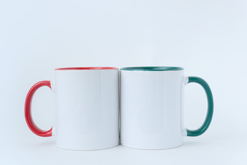 Two white mugs, with a green and red handle on a light background. 