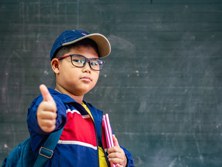 Happy Boy wear glasses smiling and stand in front of the blackboard. Back to School, Education Concept.