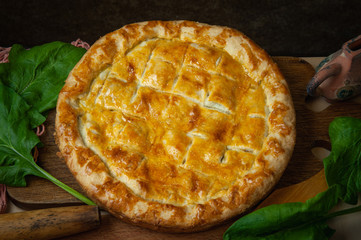 Vegetable pie homemade baking with spinach and onions, on a dark wooden background