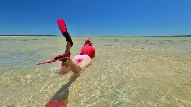 back side view of happy lifestyle woman with snorkeling wetsuit, mask and fins pink and peach color, sunbathing lying in a natural pool of Little Lagoon in Shark Bay, Denham, Western Australia.