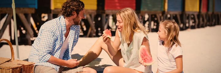 Happy family eating watermelon on blanket at beach