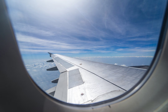 Wing of airplane flying above the clouds in the blue sky background through the window.