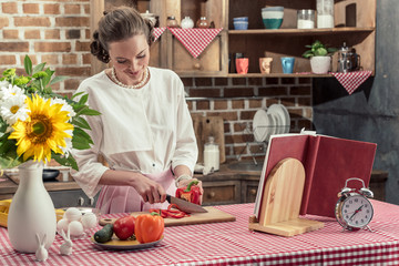 smiling adult housewife cutting bell pepper at kitchen