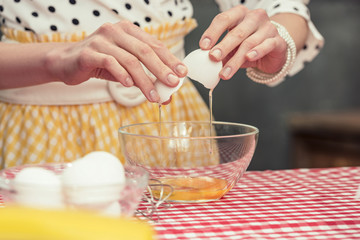 cropped shot of housewife in polka dot shirt breaking egg into bowl for omelette