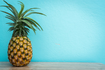 close up of pineapple on wooden table with turquoise mint cement wall background