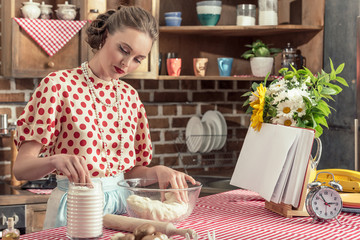 attractive adult housewife kneading dough in bowl at kitchen