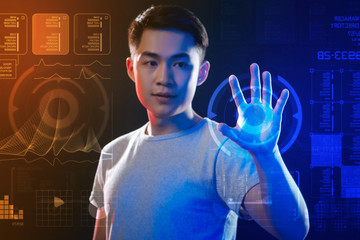 Careful programmer. Calm attentive young programmer thoughtfully looking at the round illuminated icon while putting his hand on the hologram