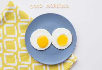 two eggs on a plate and a yellow napkin, inscription Good Morning