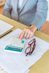 senior working woman touching calculator with eyeglasses and report data on wood desk in office