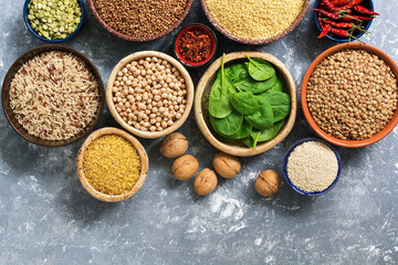 Fototapeta na wymiar A source of vegetarian protein and vitamins , a variety of cereals,beans,herbs,nuts. Chickpeas, rice,buckwheat,bulgur,lentils, peas and spinach leaves. Top view, gray background