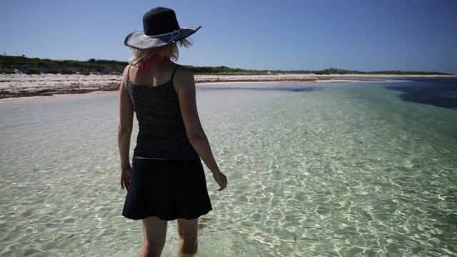 back side of woman walking in the sea water of pristine and white sand in Hangover Bay, Nambung National Park, Western Australia. Blonde girl happiness walk. Copy Space.