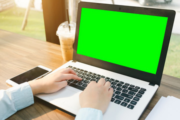 Close-up of business female working with laptop with blank green screen make a note document and smartphone in coffee shop like the background.