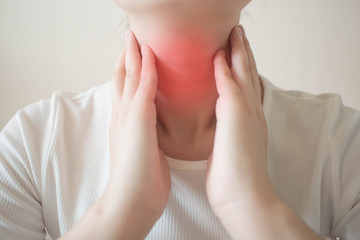 Female checking thyroid gland by herself. Close up of woman in white t- shirt touching neck with...