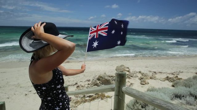 Woman on the sand looking at the turquoise sea waving Australian Flag. Mettams Pool in Trigg Beach, North Beach neighborhood near Perth, Western Australia. Tourism in Oceania.