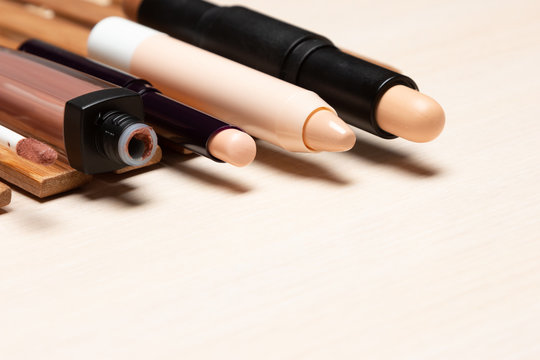 Various makeup concealers on light wood table with copy space