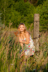 Beautiful young woman standing in a field near a concrete pillar, green grass and flowers. Outdoors Enjoy nature. Healthy smiling girl standing in tall grass