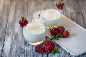Yogurt with strawberry on wooden gray table.