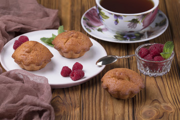 Muffin with raspberries and sugar powder on the table with tea teapot.