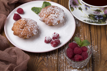 Fototapeta na wymiar Capcake with raspberries and sugar powder on the table with tea teapot.